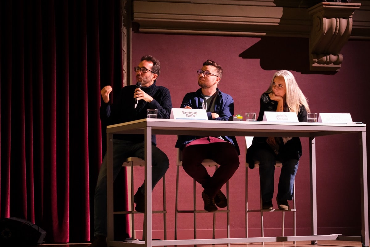 Mesa redonda con tres profesionales del sector audiovisual en un auditorio con iluminación colorida con Enrique Gato