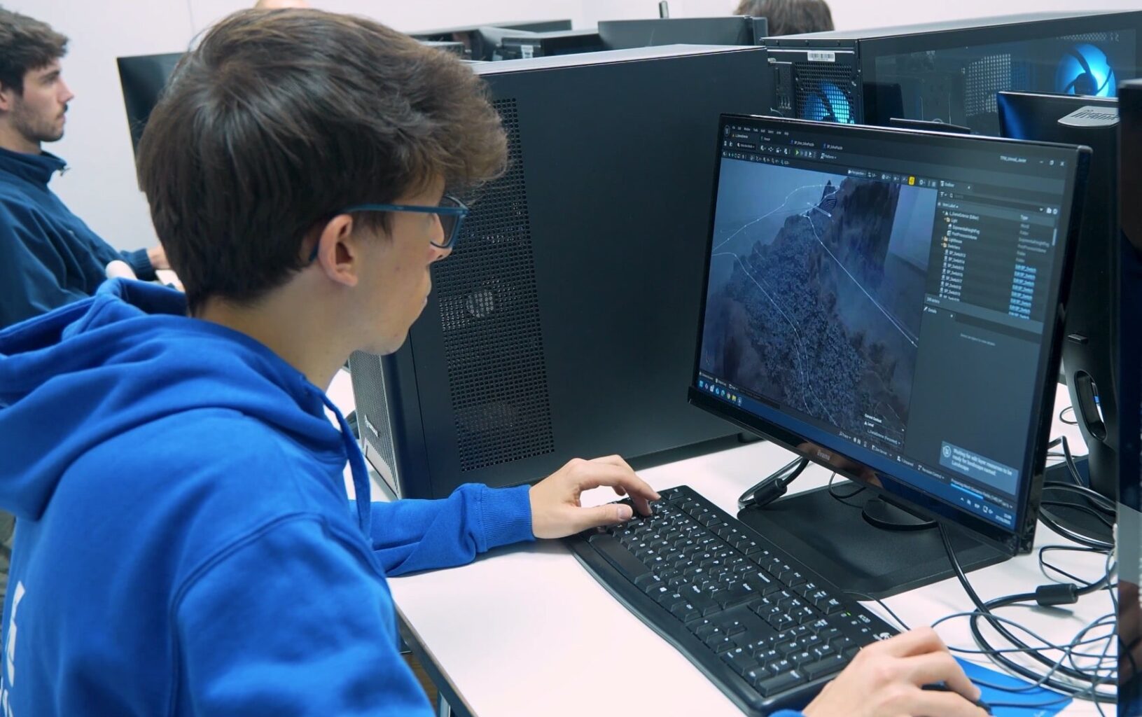Javier Atienza Pastor con sudadera azul trabajando en un ordenador de sobremesa, editando un entorno 3D en pantalla
