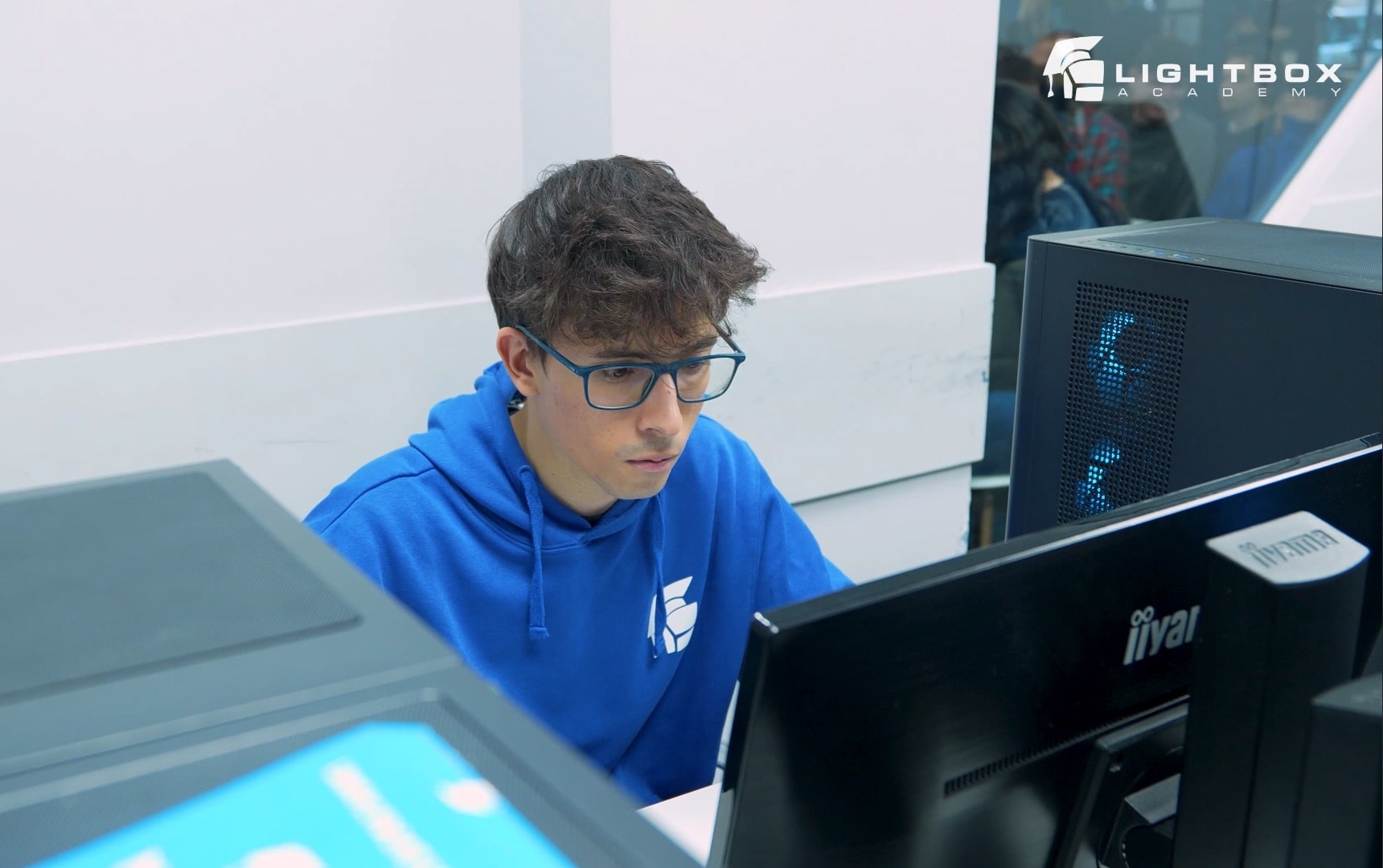 Javier Atienza Pastor con sudadera azul concentrado frente a un monitor en aula informática con logo de Lightbox Academy.
