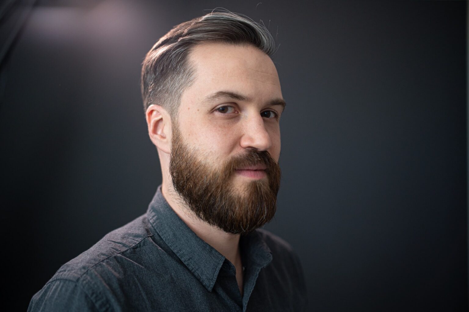 Retrato de perfil de Szymon Biernacki con barba y pelo canoso peinado hacia atrás, sobre fondo gris neutro.