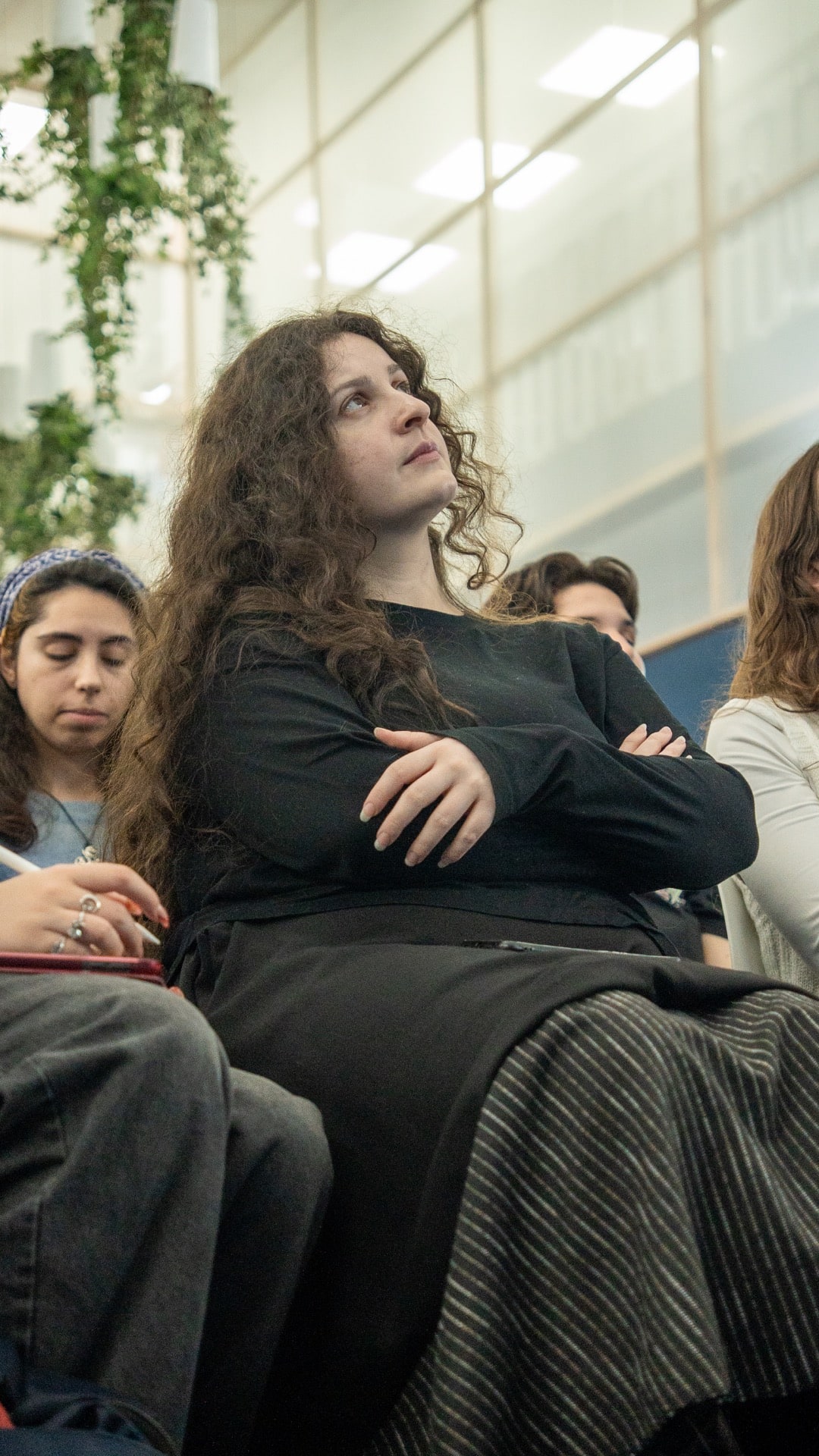 Alumna sentada con los brazos cruzados y expresión atenta, rodeada de otros estudiantes tomando notas en la masterclass.